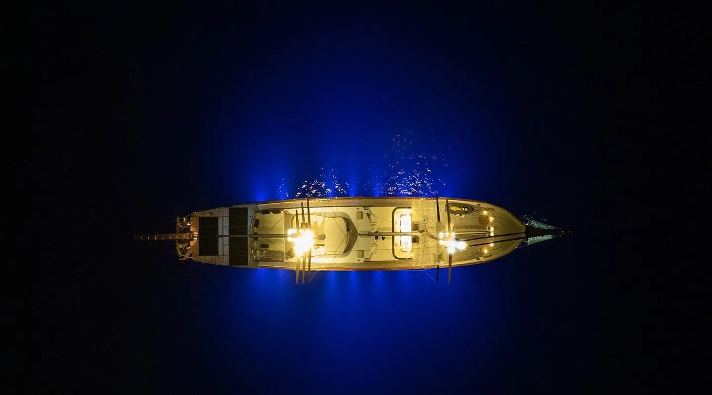 Gulet yacht Double Eagle at night, illuminated amidst dark blue sea