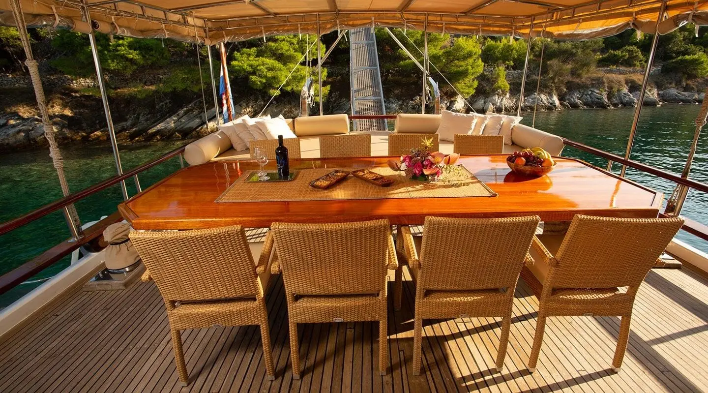 Luxurious Malena yacht charter table on deck at sunset with wicker chairs