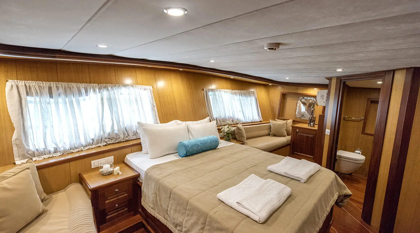 Kayhan 3 yacht interior with bed, towels, and wood paneling under cabin lighting