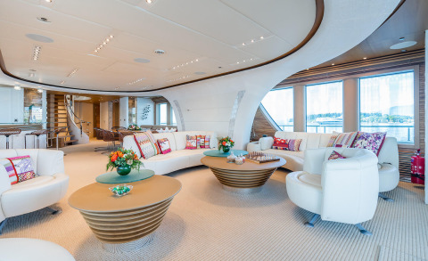 Serenity yacht interior: white curved seating, colorful cushions, round wooden coffee tables, large windows with water view