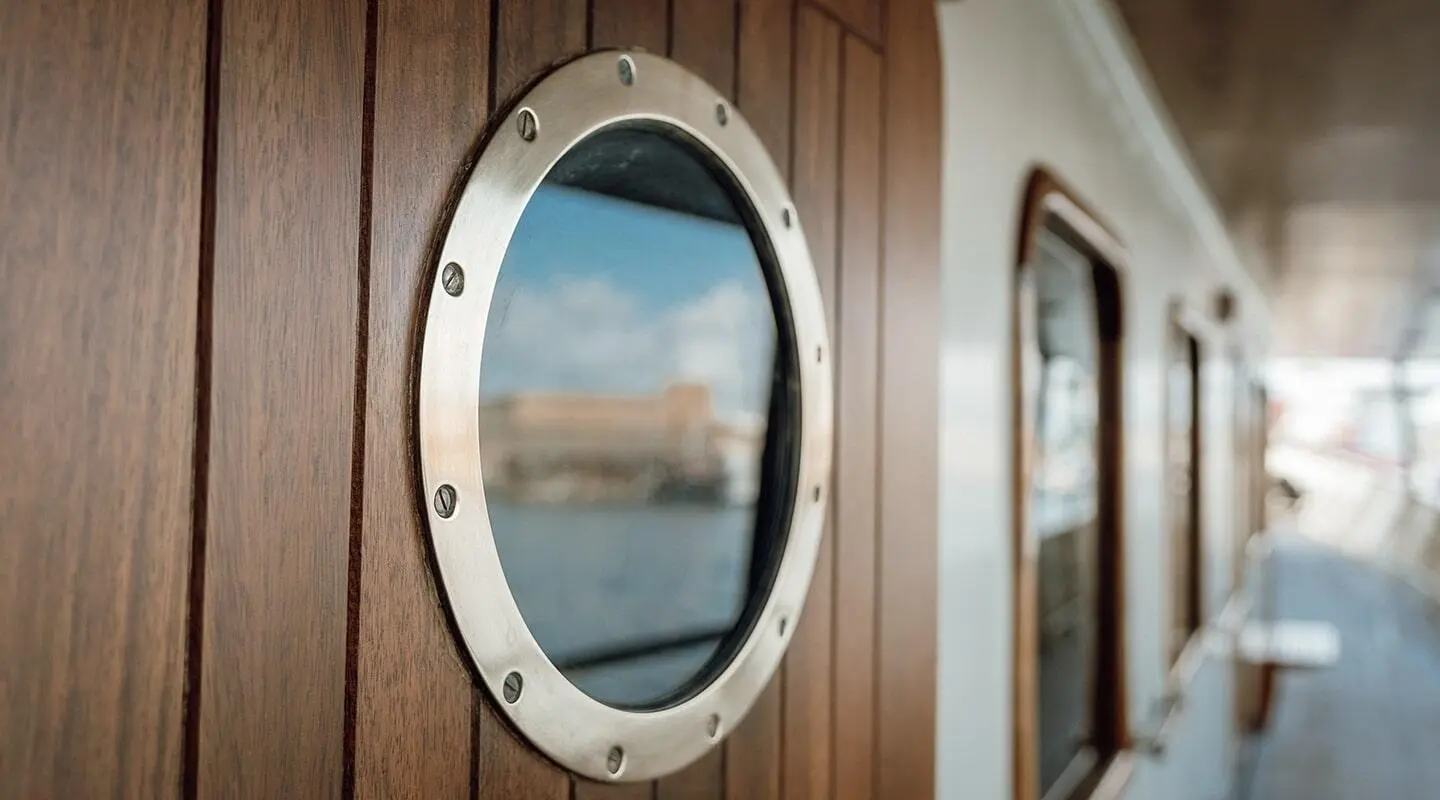 Seagull II yacht deck window with round porthole and wooden trim, reflection