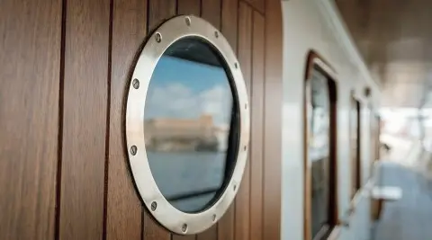 Seagull II yacht deck window with round porthole and wooden trim, reflection