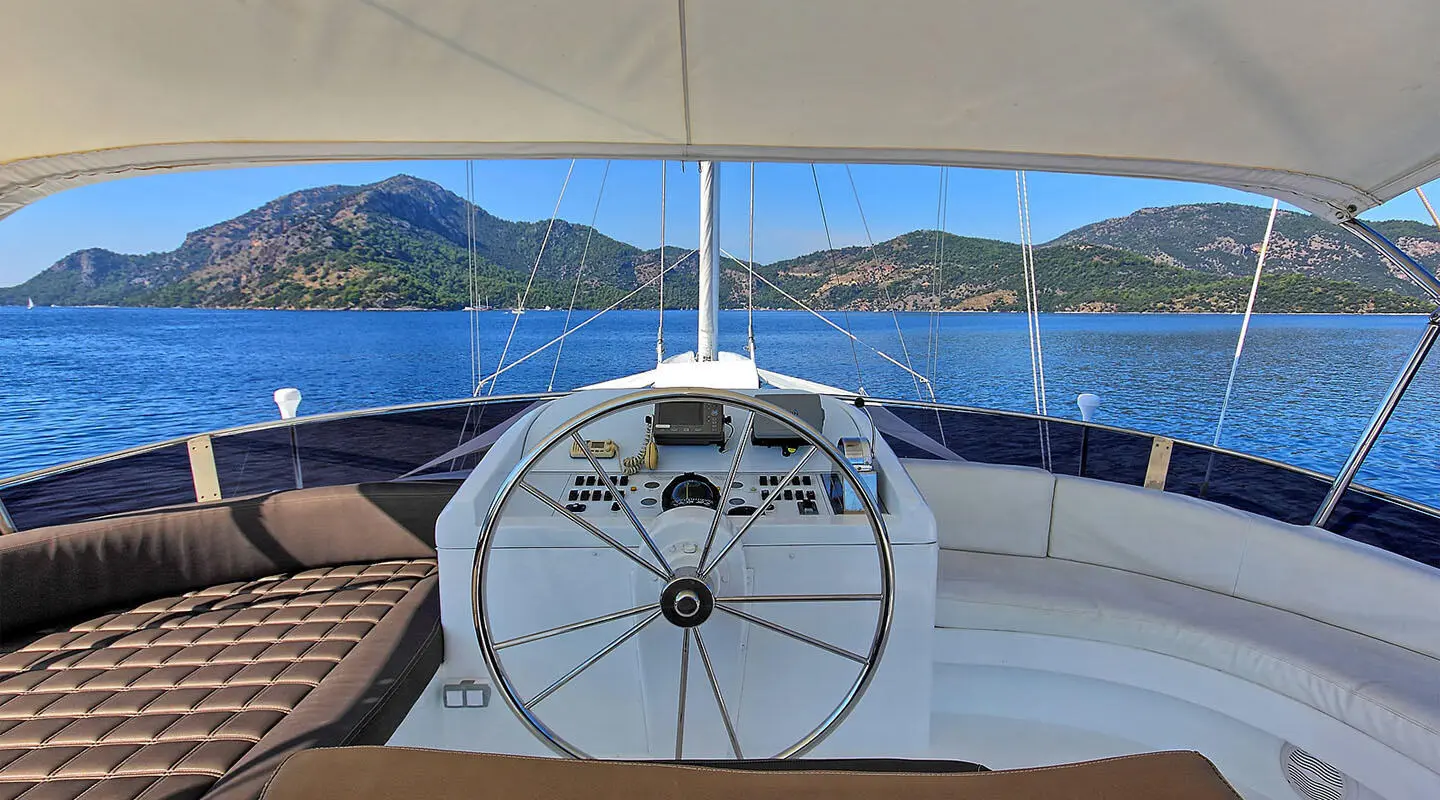 Angelo II yacht helm steering wheel on deck with blue sea and hills in background