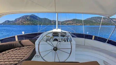 Angelo II yacht helm steering wheel on deck with blue sea and hills in background