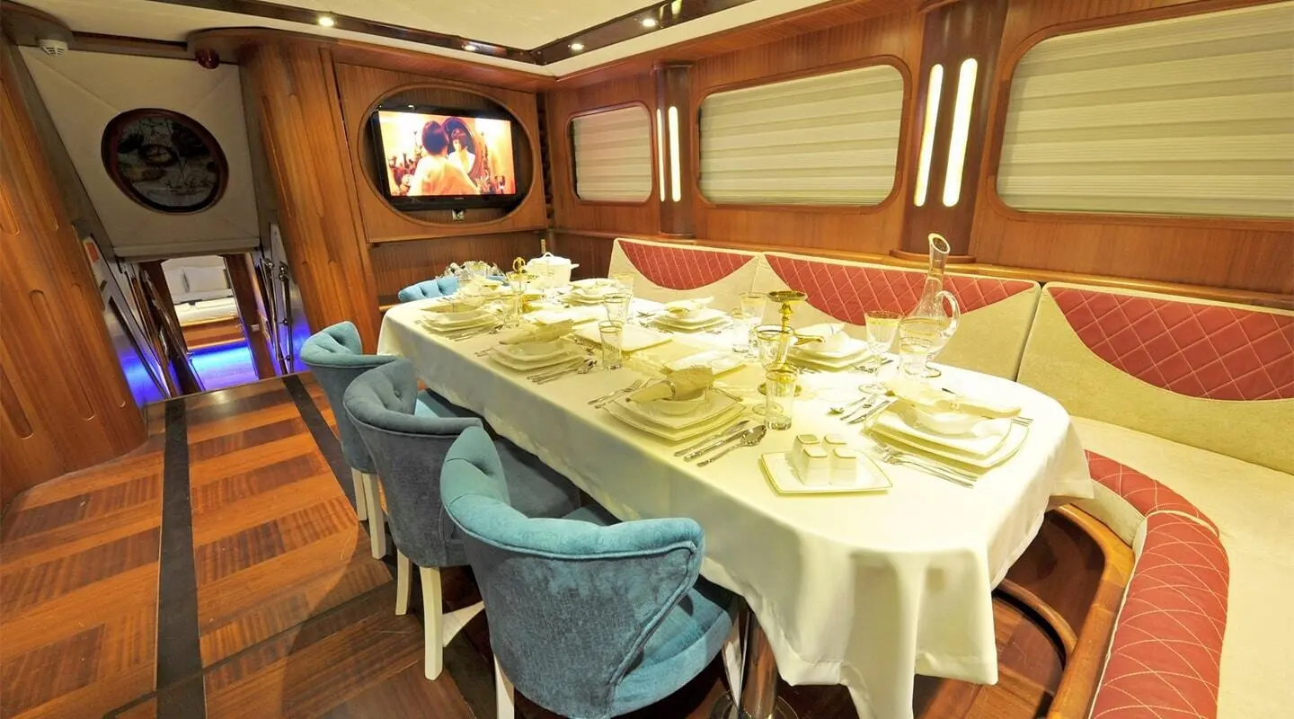 Indoor dining area on a luxury yacht with a long table set for dinner and blue chairs