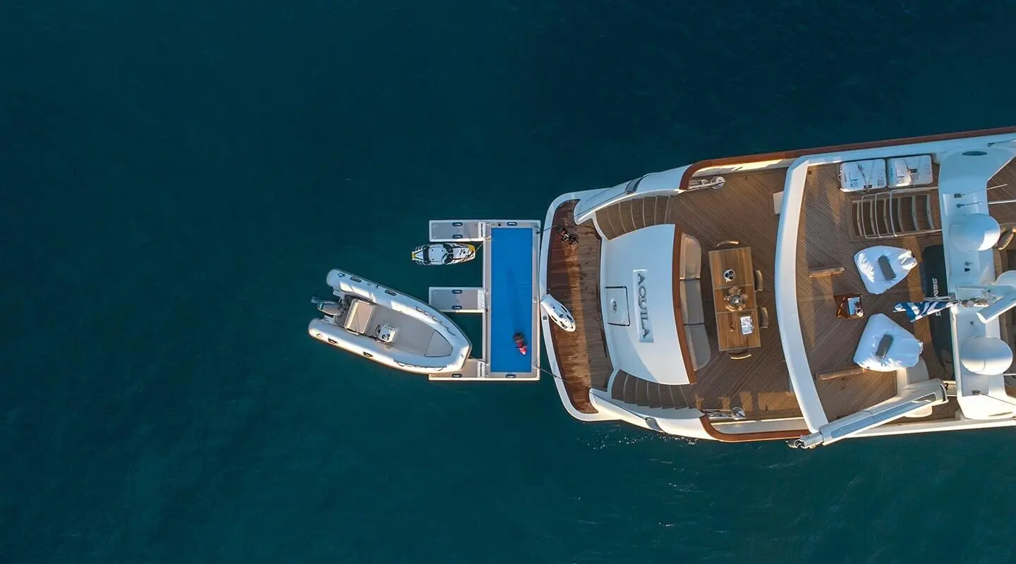 Aquila yacht seen from above with a small tender nearby in turquoise water