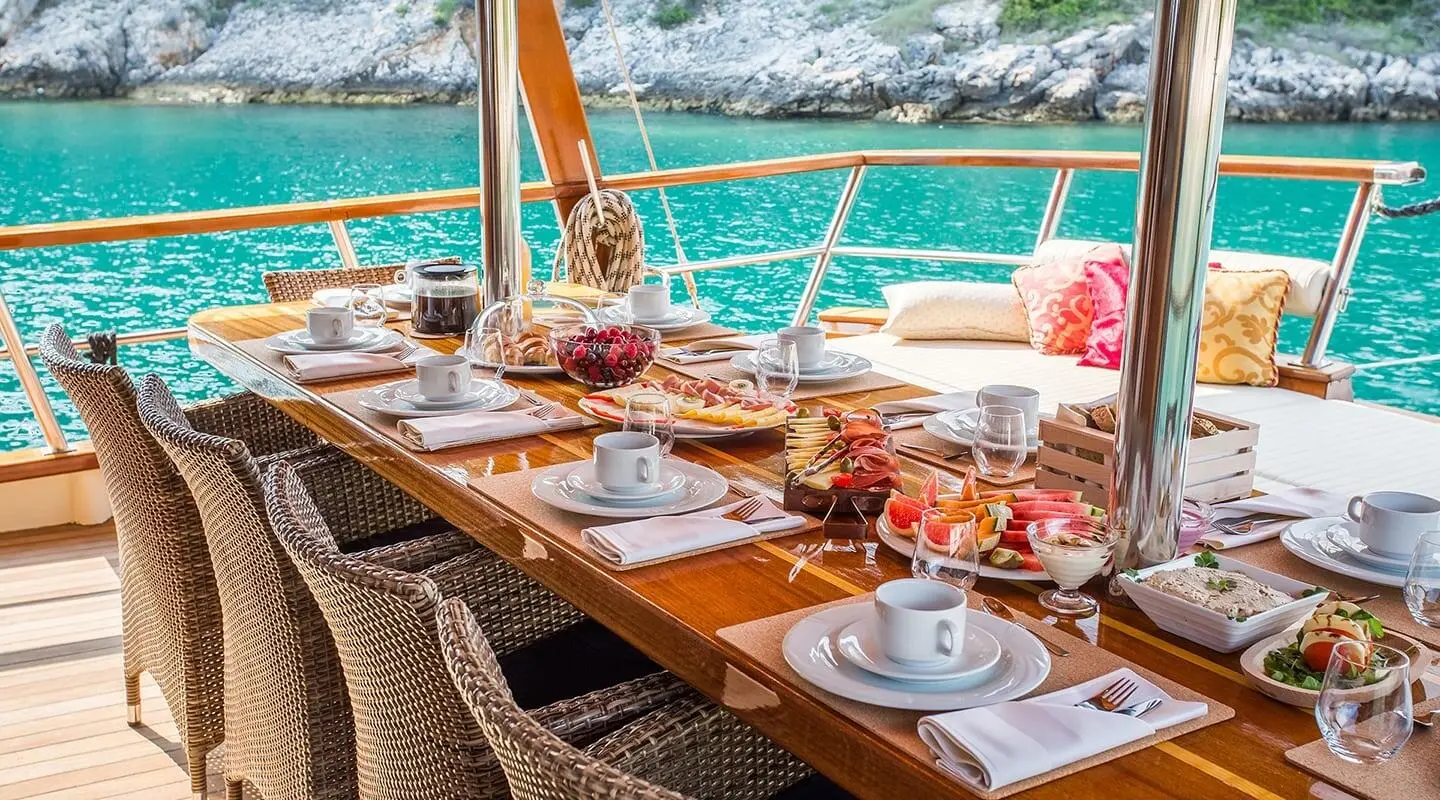 Sunset onboard Altair yacht with a long dining table set for guests and turquoise sea in background