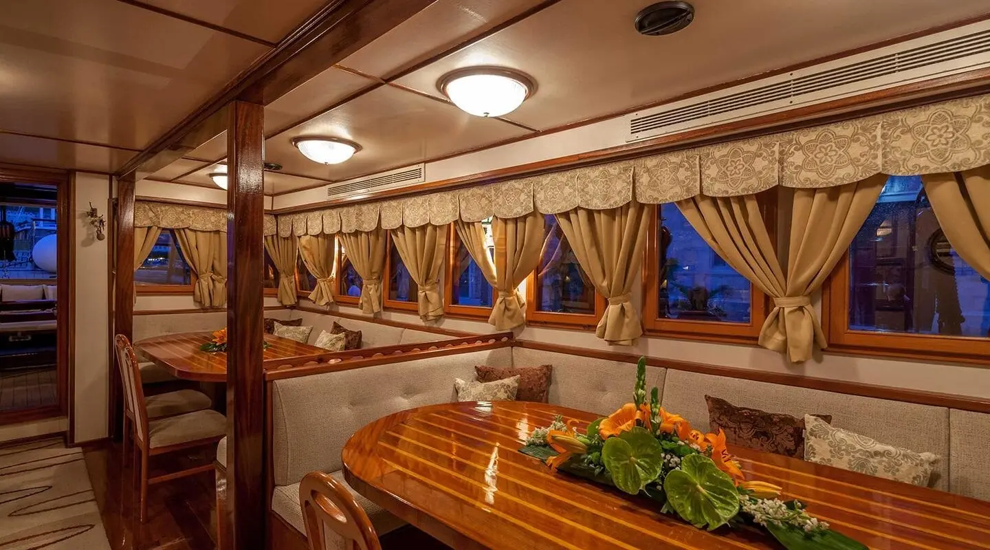 Romanca yacht charter interior with wooden table, seating, and blue curtains