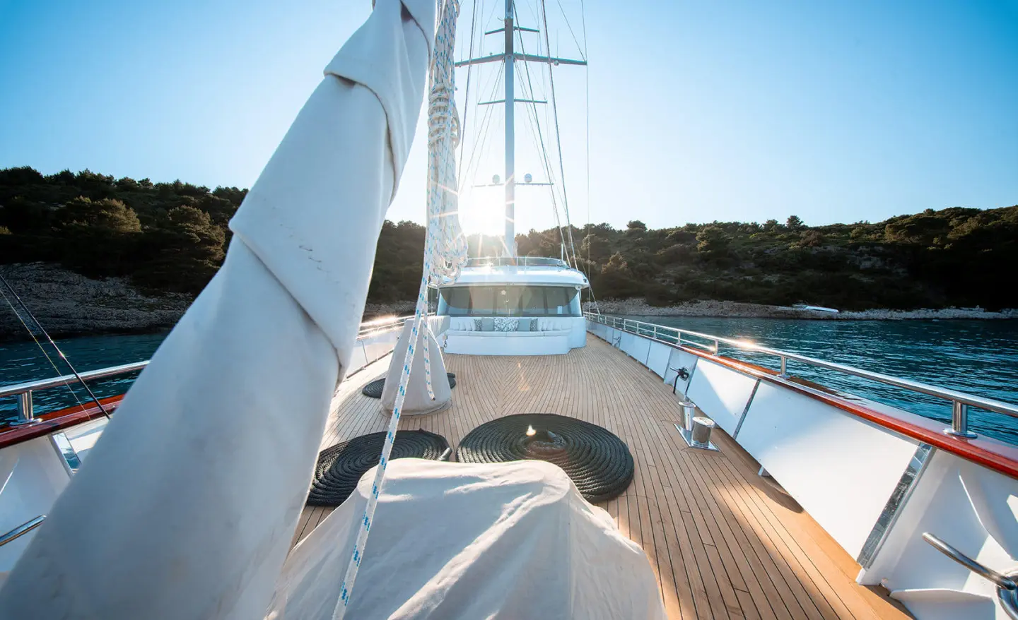 Nocturno yacht bow deck with railing, sunlit wood, and blue horizon