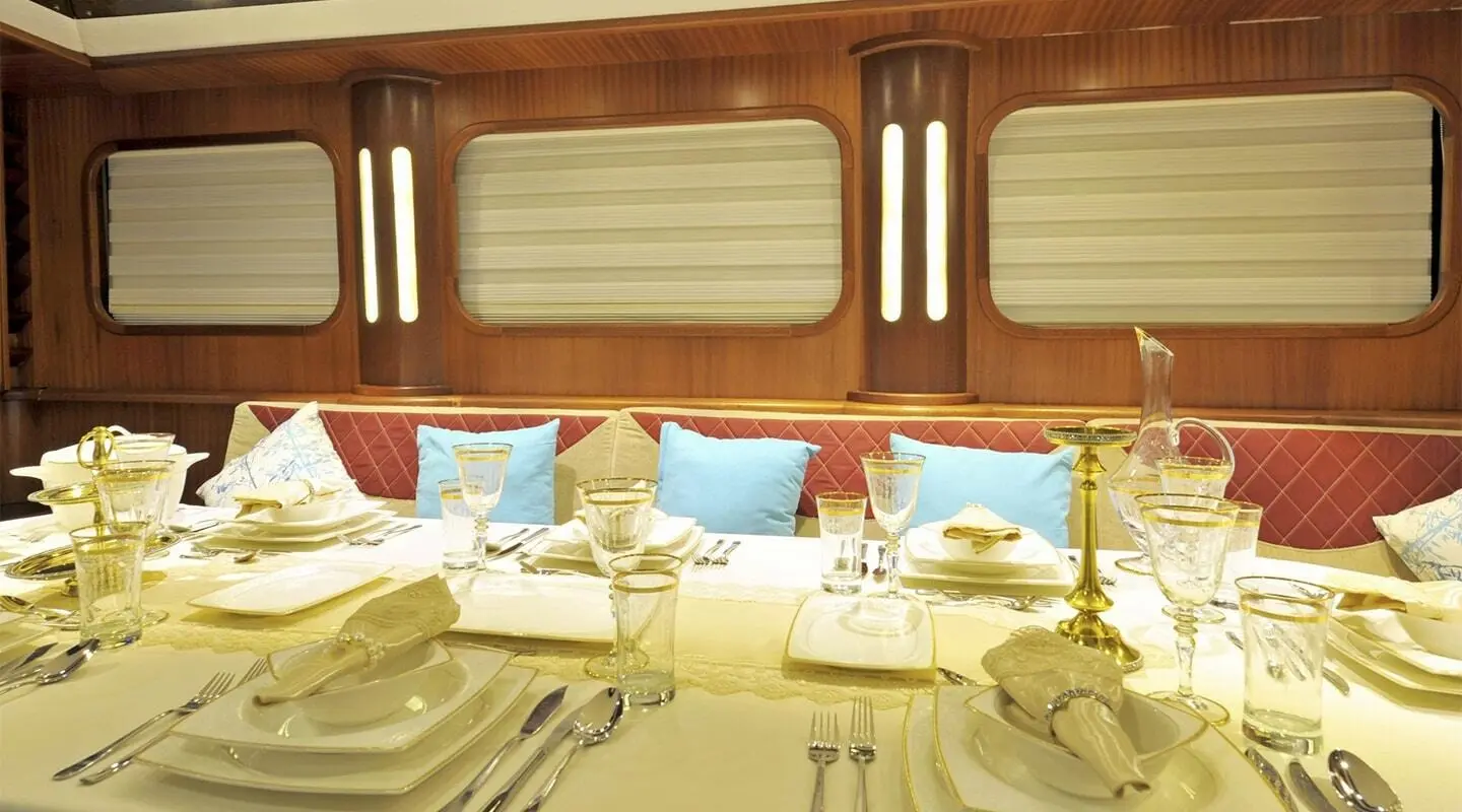 Luxurious yacht Berrak Su dining area aboard, sunlit teak interior with cushions