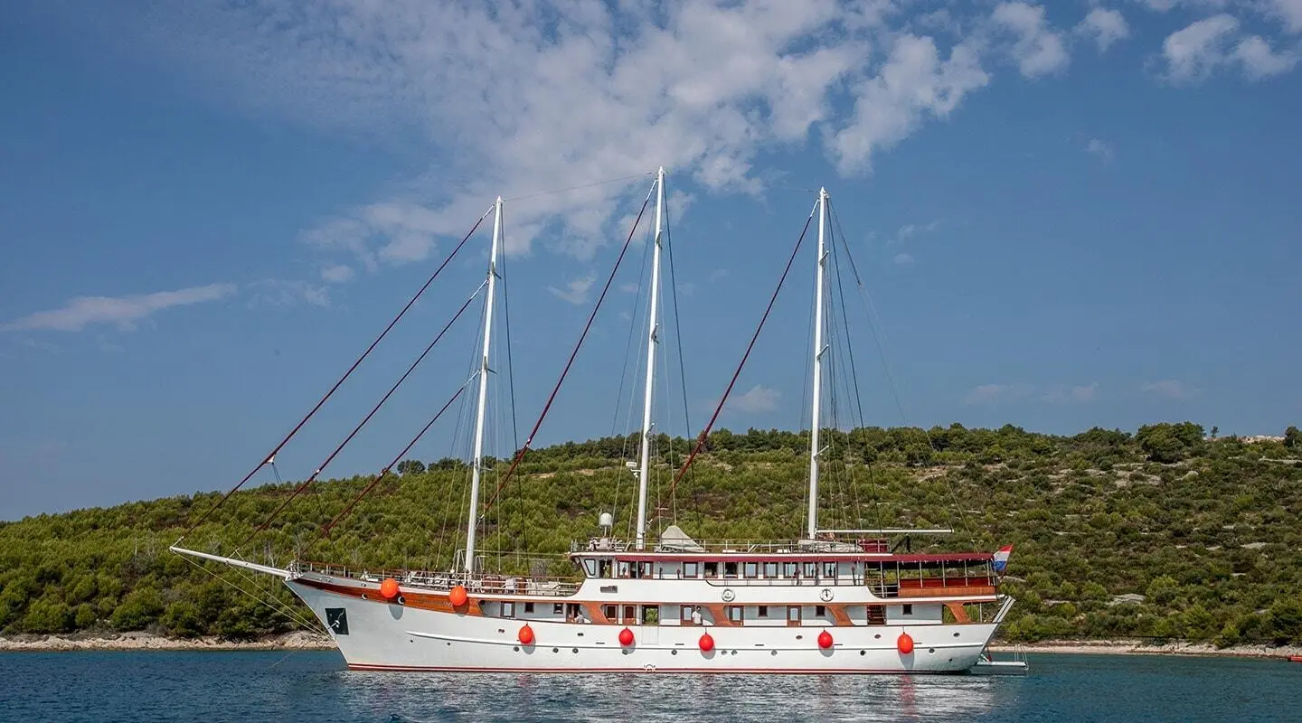 Side view of Amorena motoryacht with sails, anchored near a hillside