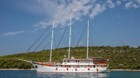 Side view of Amorena motoryacht with sails, anchored near a hillside