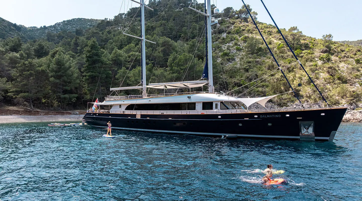 Dalmatino luxury yacht moored near a rocky coastline with hills in the background