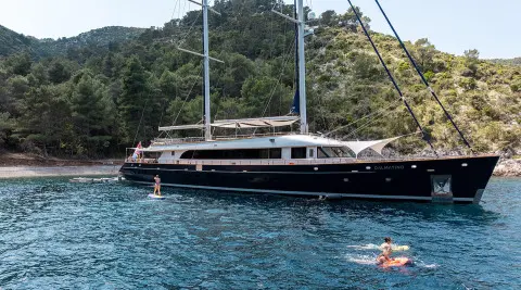 Dalmatino luxury yacht moored near a rocky coastline with hills in the background
