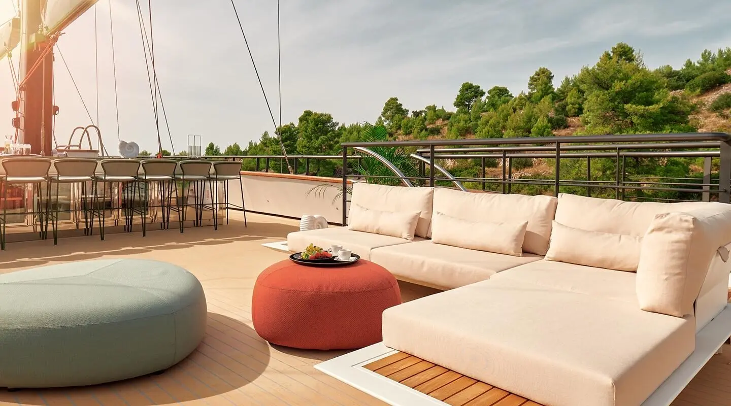 Anetta yacht deck area with cream and red cushioned seating and a glass railing at sunset