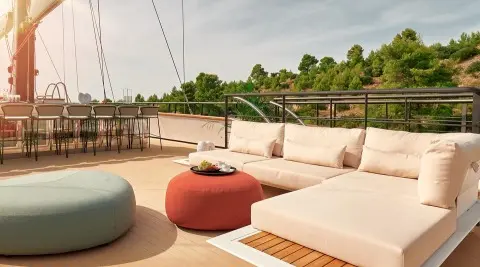Anetta yacht deck area with cream and red cushioned seating and a glass railing at sunset