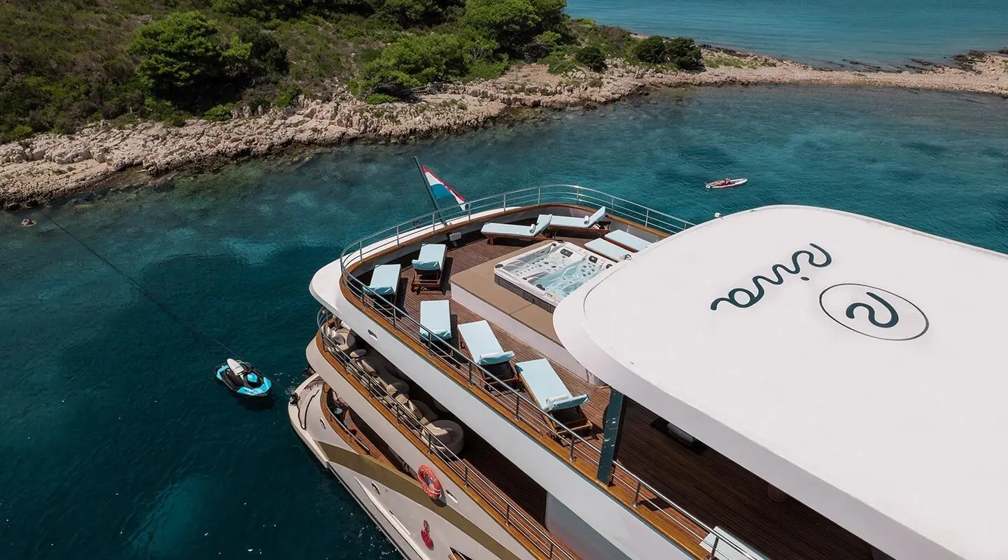 Yacht Riva anchored near rocky coastline with people on deck and sunshade