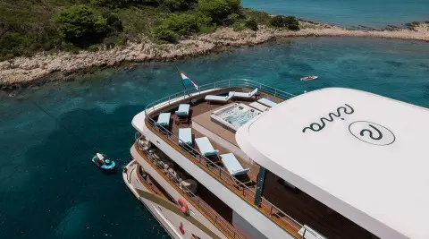 Yacht Riva anchored near rocky coastline with people on deck and sunshade