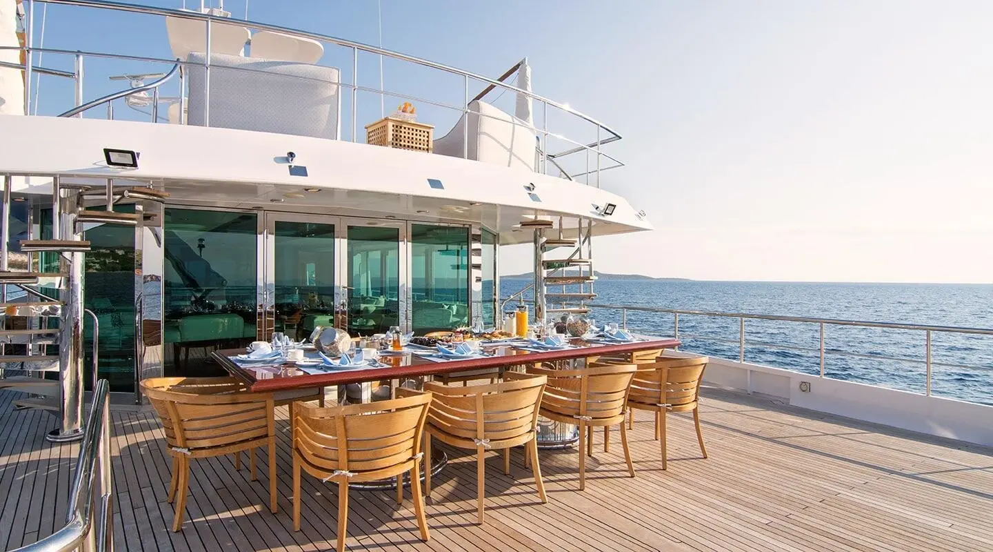 O'Natalina yacht dining deck with wooden table set and ocean view at sunset