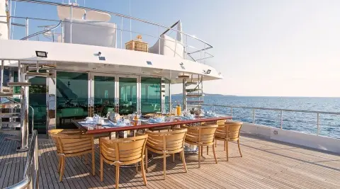 O'Natalina yacht dining deck with wooden table set and ocean view at sunset