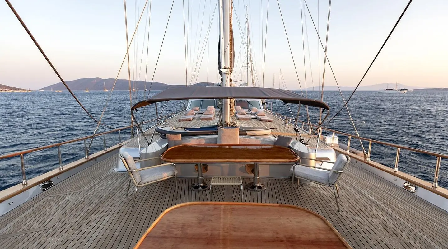 View from the aft deck of a luxury gulet at sunset, wooden seating and table