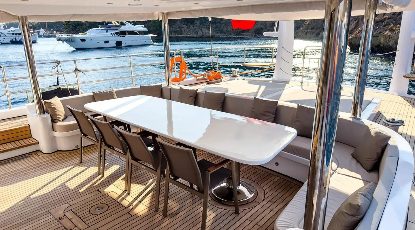 Angelo III yacht deck with white table and chairs under canopy, sunset harbor view