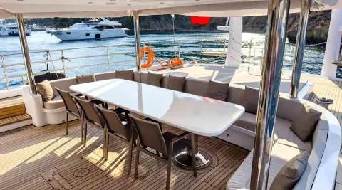 Angelo III yacht deck with white table and chairs under canopy, sunset harbor view