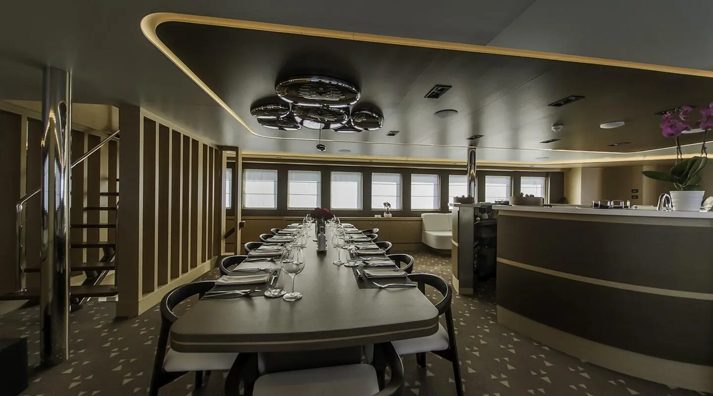 Omnia yacht interior: elongated dining table set for guests in a luxurious lounge