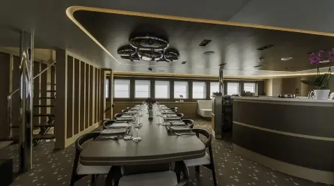Omnia yacht interior: elongated dining table set for guests in a luxurious lounge