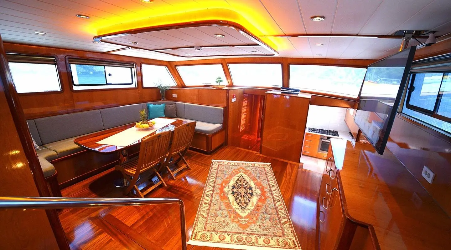 Maya yacht interior: wooden deck, cushioned seating, table, warm lighting, and stairs