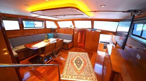 Maya yacht interior: wooden deck, cushioned seating, table, warm lighting, and stairs
