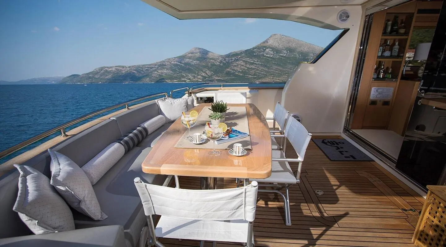 Salt yacht deck dining area with wooden table and seating, blue sea view