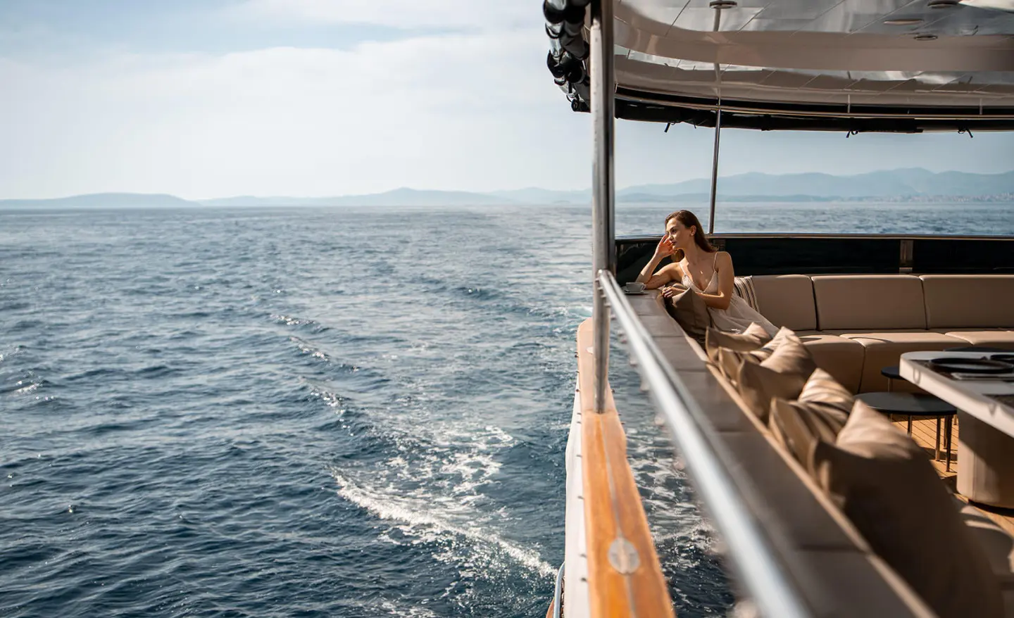 Yacht Cristal cruising on calm blue sea, passengers leaning on railing on sunny day