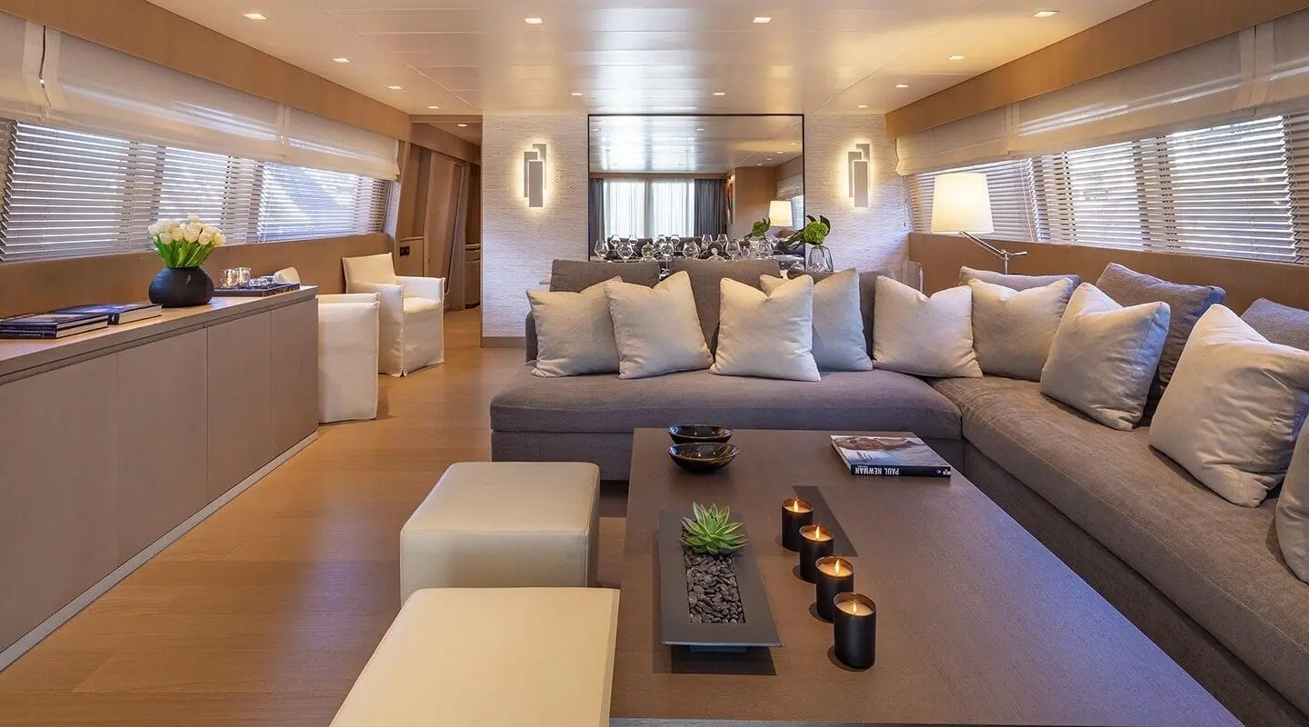 Inside of a yacht salon with a large L-shaped sofa, cushions, and a central coffee table