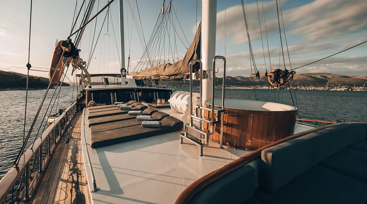 Luxurious Croatia sailing yacht deck with sun loungers and teak, sunset harbor backdrop