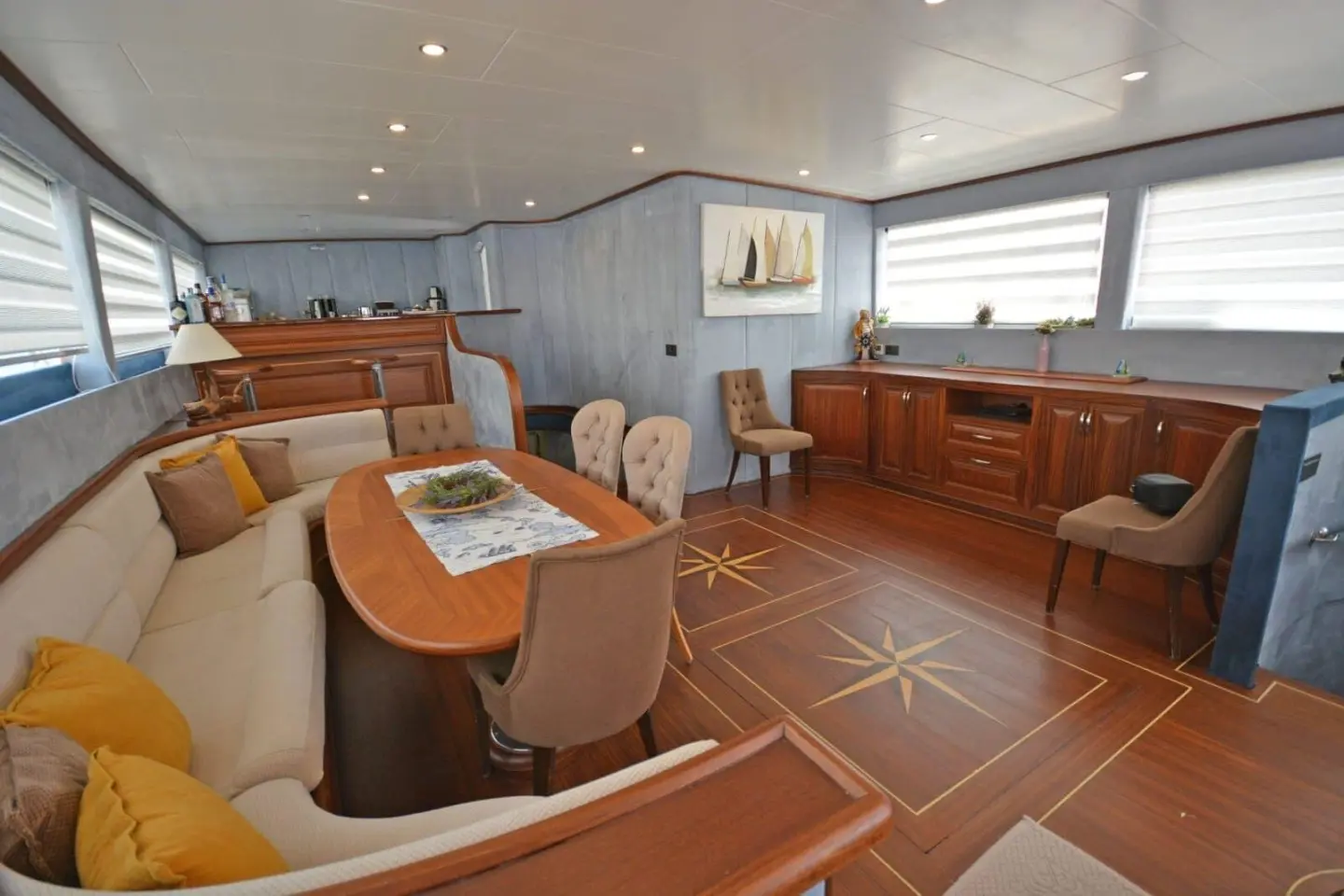 Interior of Bella Mare yacht with cushioned seating, wooden accents, and helm station under windows