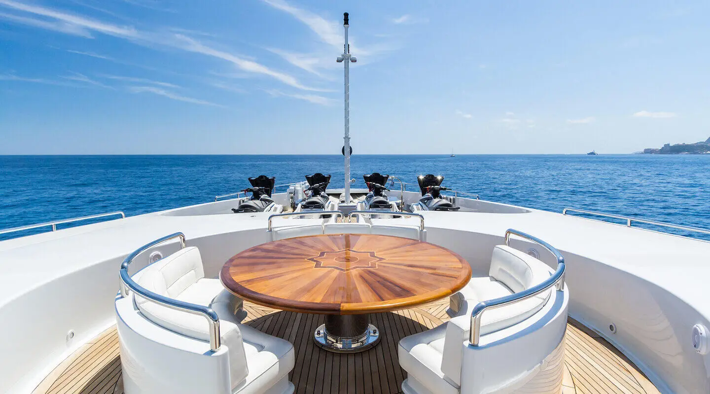 On the yacht Apogee, wooden round table with chairs on the bow deck, ocean view