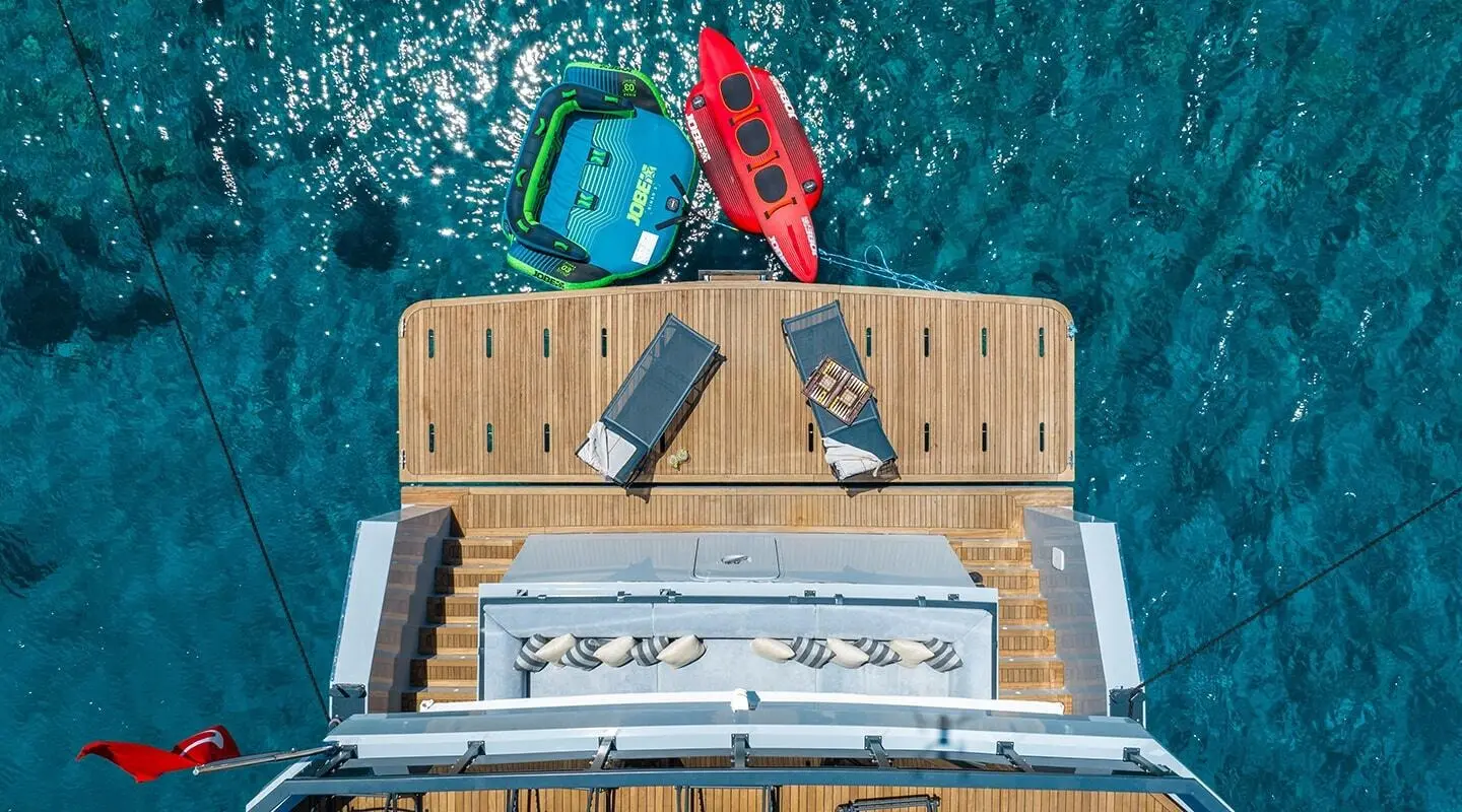 Top-down view of a boat deck with lounge area and swim platform in turquoise water